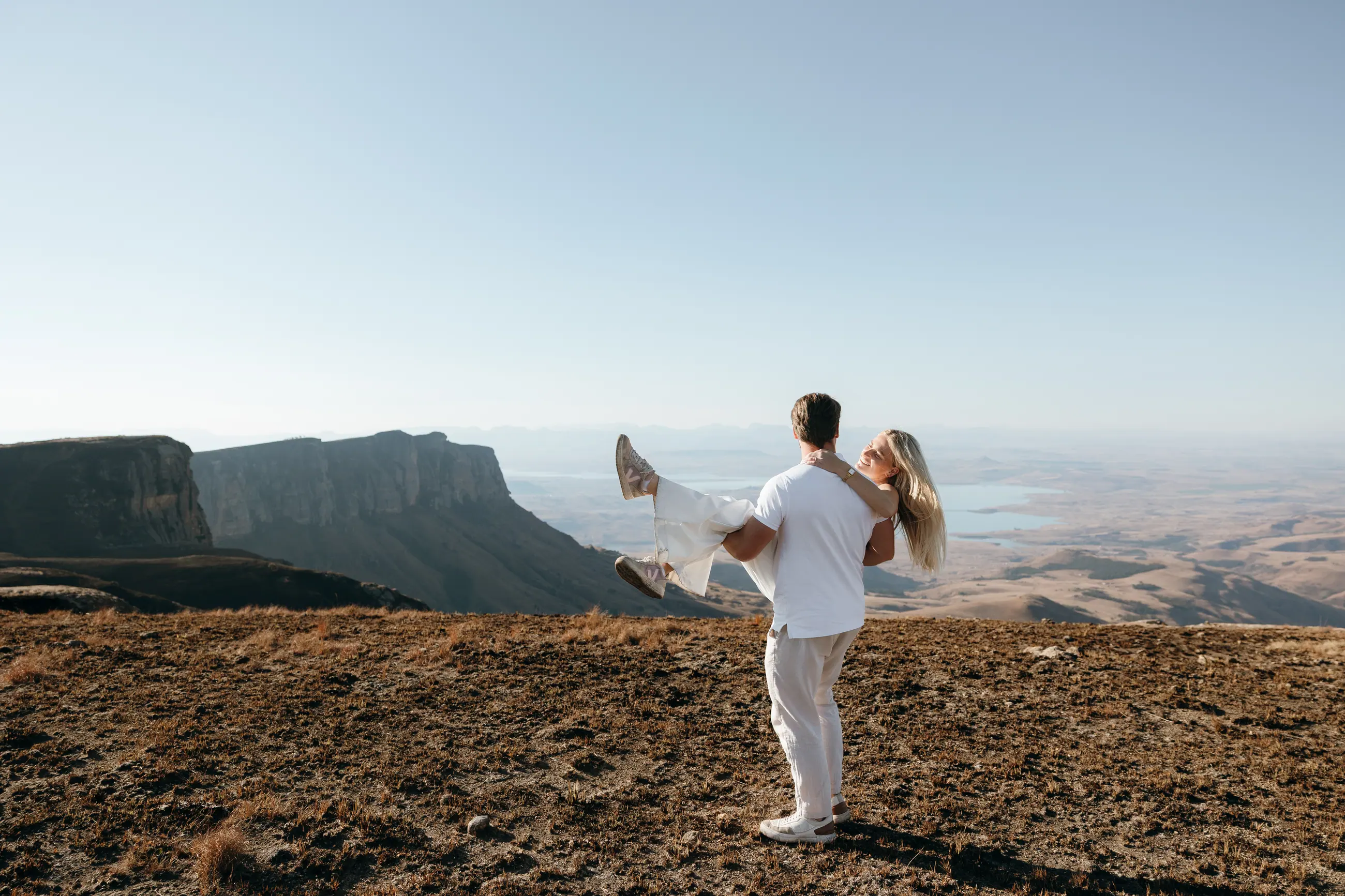 Christy and Joshua embracing on the escarpment edge with mountains behind them