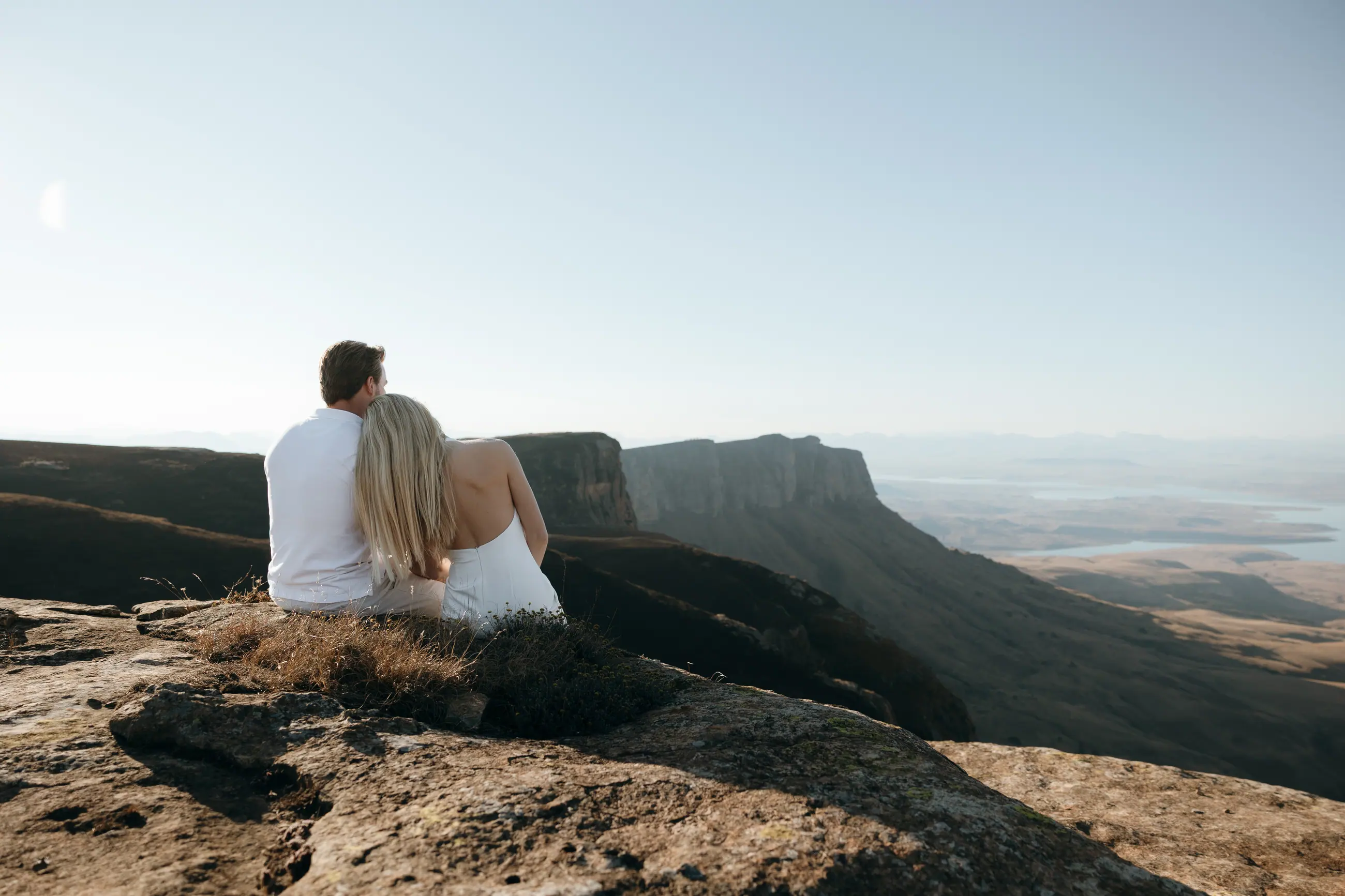 Christy and Joshua sitting together on a mountain ridge, looking out over the valley